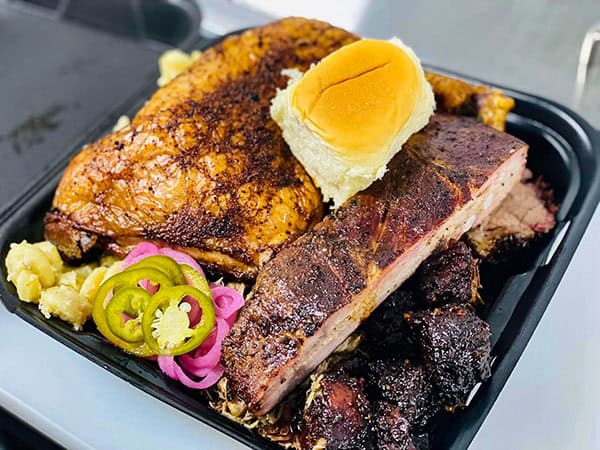 Jay’s Smokin BBQ pit plate with 3 smoked meats, Gouda mac and cheese, and a corn bread bun
