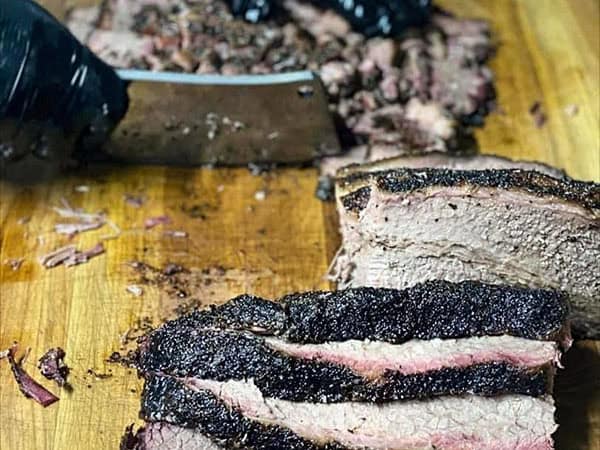 Texas-style smoked brisket getting cut on a wood cutting board at Jay’s Smokin BBQ at Muscle Car City in Punta Gorda
