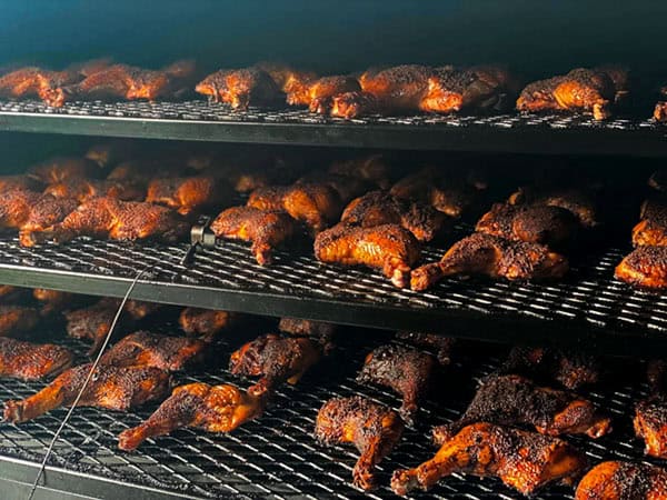 Racks of smoked chicken thighs rotating through wood smoker at Jay’s Smokin BBQ at Muscle Car City in Punta Gorda